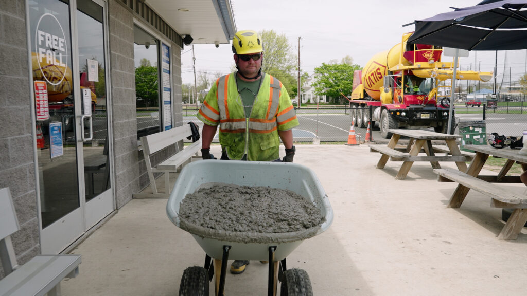 A construction worker transporting concrete in a wheel barrow to a pour location.