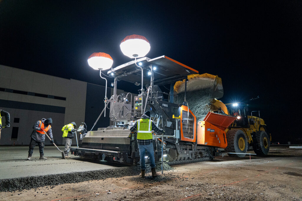 Roller-compacted concrete being placed with a specialized RCC paver during an industrial paving project.