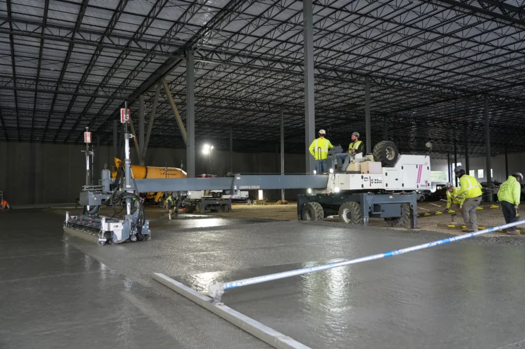 Construction crew using a laser screed to level freshly placed concrete during a large industrial warehouse floor pour.