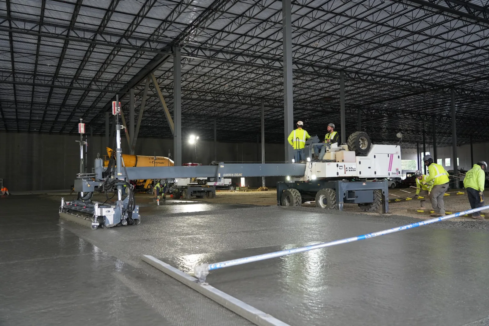 Construction crew using a laser screed to level freshly placed concrete during a large industrial warehouse floor pour.